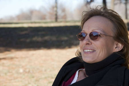 A woman with a passing car reflecting in her sunglasses, sitting in grass watching the world go by. の写真素材