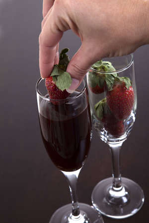 Female hand dipping a strawberry into a champagne flute filled with chocolate to make a sensual snack.の写真素材