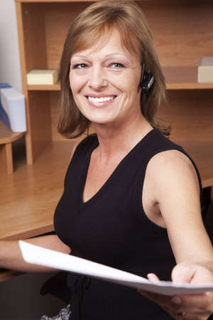 A female office employee handing someone papers while sitting at her desk.の写真素材