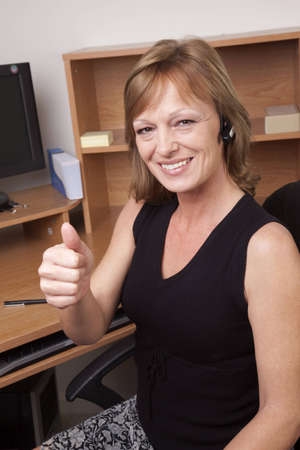 A business woman giving a thumbs up sign at her office deskの写真素材