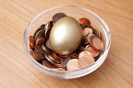 A golden egg laying in a bed of coins in a bowl as if a nest eggの写真素材