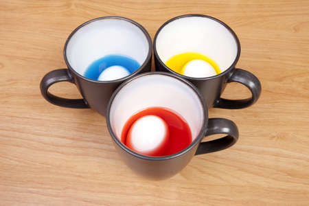 Eggs being colored in coffee cups on a desk. Arrangement of cups appears like a smiley face. の写真素材