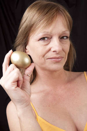 Mature woman secure in her investments symbolized by golden eggの写真素材
