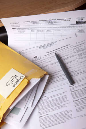 Unpaid bills in a yellow envelope on a stack of tax forms for corporate dissolution on a desk. の写真素材