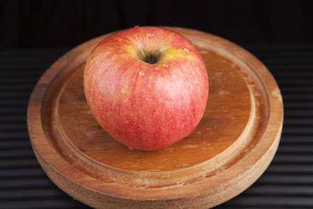 A red apple on a wooden serving platter against a black background. の写真素材