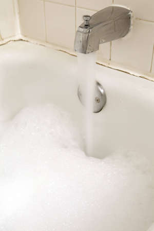 Long exposure of water flowing from a faucet into an aged tub full of bubbles.の写真素材