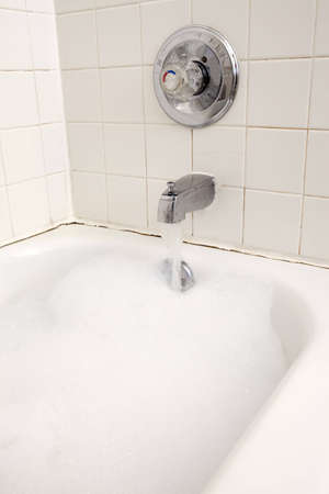 Long exposure of water flowing from a faucet into an aged tub full of bubbles.の写真素材