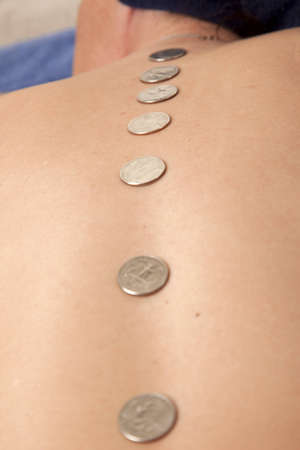A line of coins down a womans back, like hotstone therapy. Healing money worries with quarters.の写真素材