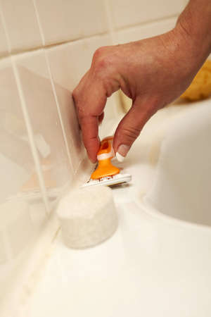 A hand reaching to pick up a razor on the edge of a bath tub.の写真素材