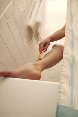 A woman in the shower shaving her leg. Low angle closeup up shot of leg and armの写真素材