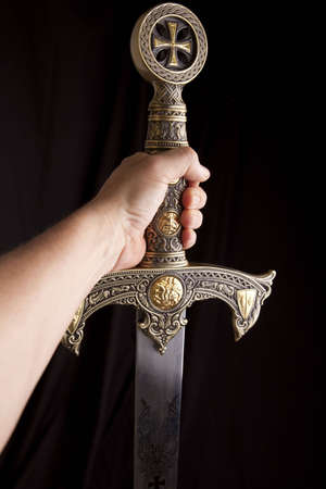 Arm holding out a knights ornate sword in a dramatic dark scene