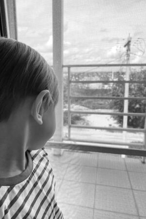 the boy stays at home and looks out the window. boy misses his friends and classmates. During quarantine, children sit at home in isolation.の写真素材