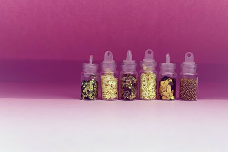 Colorful glitters for nail art and makeup in small glass jars isolated. Fashion and beauty concept, pink backgroundの写真素材