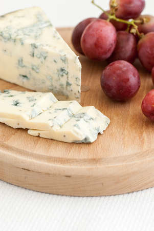 tasty sliced moldy cheese and red grapes on wooden plateの写真素材