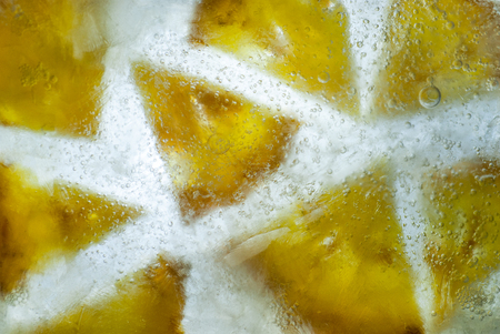pineapple slices cut in quarters frozen in ice with back lit and air bubbles stuck abstract concept background photoの写真素材