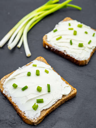 slices of bread with cream cheese spread and fresh green onion on black slate breakfast shack conceptの写真素材