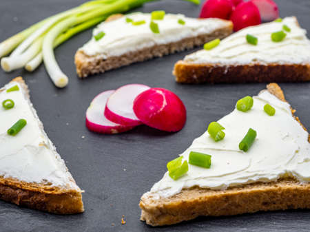 slices of bread with cream cheese spread and fresh green onion on black slate breakfast shack conceptの写真素材