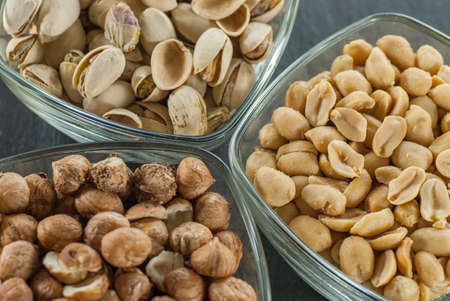 bowls with assorted nuts like hazelnuts pistachio and peanuts on black slate healthy life concept