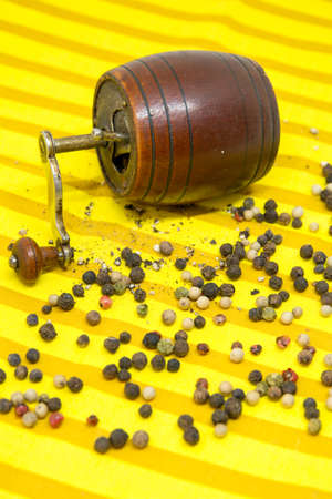 old pepper grinder and assorted pepper whole grains and ground pepper on yellow cloth