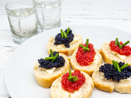 plate slices of bread with assorted fish roe and glasses of vodka asideの写真素材