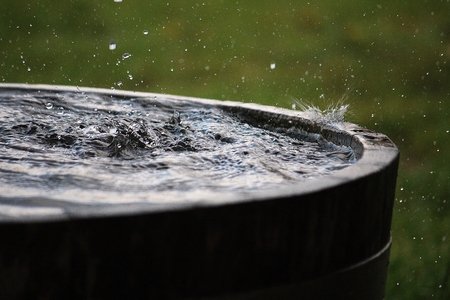 Rain is falling in a wooden barrel full of water in the garden