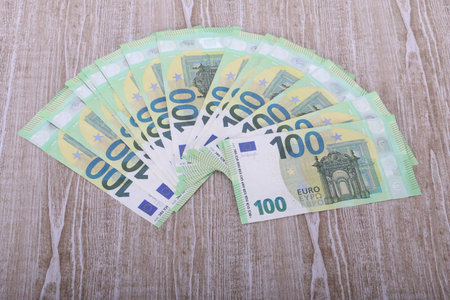 A pile of green 100 euro bills lie spread out like a fan on a wooden tableの写真素材