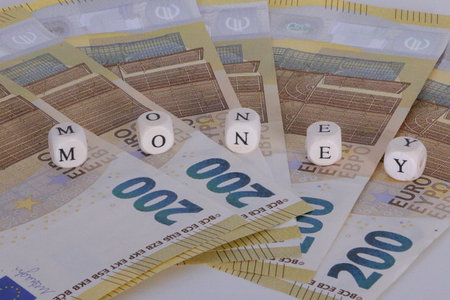 Stacks of 200 euro bills lie fanned out on the table and on them are wooden cubes with letters that...