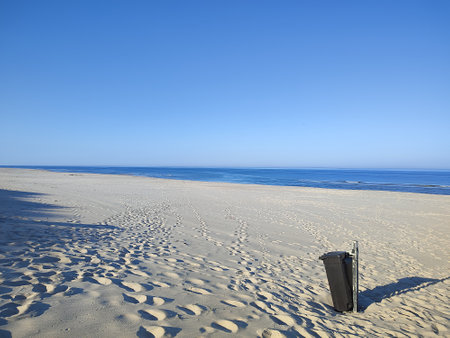 black trash can stands on a deserted beach on a sunny dayの写真素材