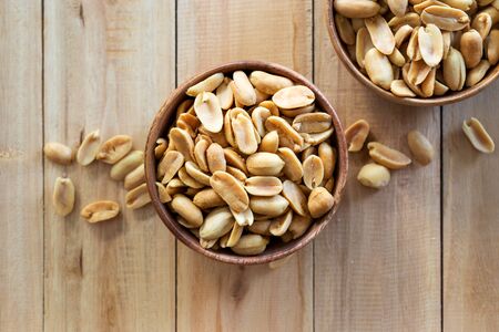 Roasted salted peanuts in white wooden bowl on wooden table background from above