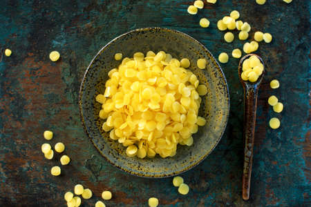 yellow beeswax pellets in ceramic plate on green grunge wooden background.