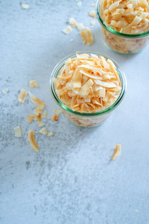 roasted crispy coconut flakes in a glass bowl on white table background.