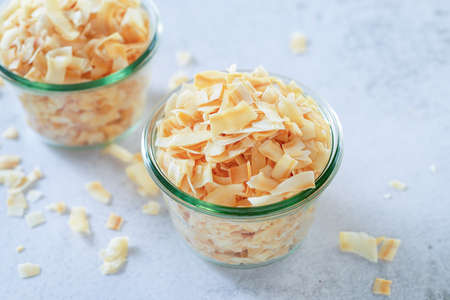 toasted crispy coconut flakes in glass bowl on white table background.