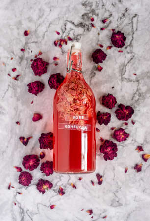 homebrew rose Kombucha in swing top glass bottle with dried rose buds on white table background.,...