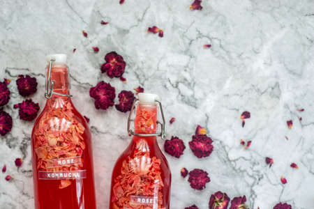 homebrew rose Kombucha in swing top glass bottle with dried rose buds on white table background.,...
