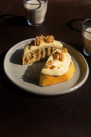 Sliced homemade mixed fruit cinnamon roll with cream cheese frosting and walnuts on top on a ceramic plateの写真素材