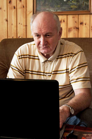 Senior man is working on laptop in living-roomの写真素材