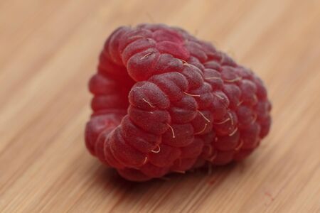 Extremely close-up view of raspberry lying on the wooden kitchen board