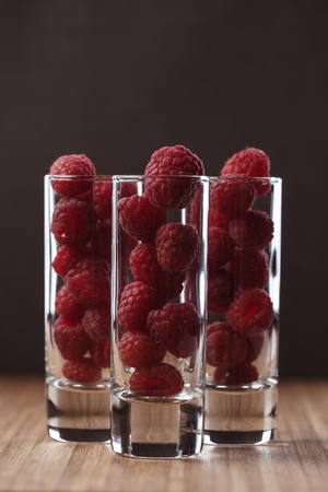 Many raspberries in three long shot glasses on the wooden board