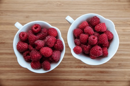 Many raspberries in white tea cups on the wooden board