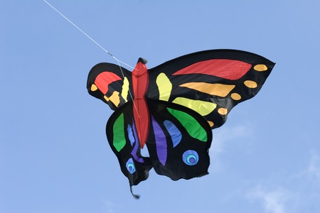 A colorful butterfly shaped kite flying in a blue skyの写真素材