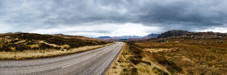 Road between fields and mountains on a cloudy day in Highlands, Scotland