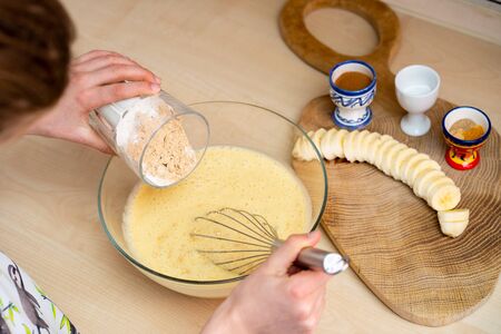 Young girl is holding a glass with flour and preparing, easy to make and healthy, home made banana bread  - during stay at homeの写真素材
