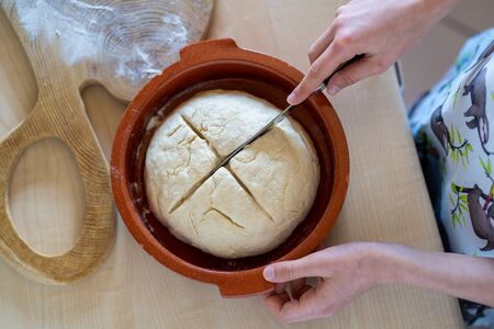 Hands of a young girl holding knife and making cross on easy to prepare and healthy, home made irish soda bread - during stay at homeの写真素材