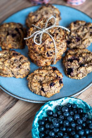 Set of easy to prepare and healthy, homemade oatmeal and blueberry cookies - on beautiful blue plate. Bowl full of blueberries next to it.の写真素材