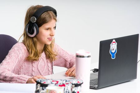 Young, blond girl in pink sweater is smiling while doing her lessons. Homeschooling during isolation...