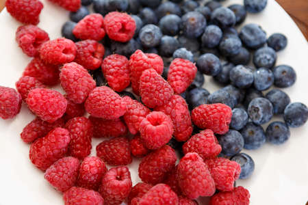 closeup of blueberries and raspberries on white plateの写真素材