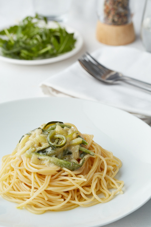 a plate of pasta with zucchini and some rocket salad in the backgroundの写真素材