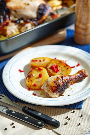 baked chicken drumstick and potatoes on the white plateの写真素材
