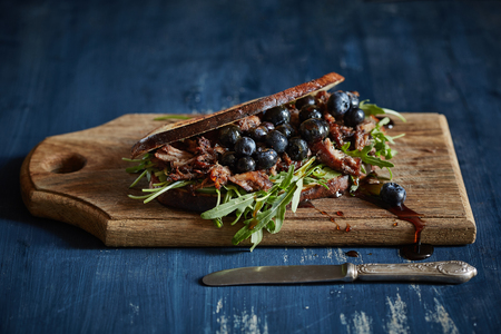 a palatable closed sandwich with roasted bacon, blueberries and arugula served on the wooden cutting boardの写真素材