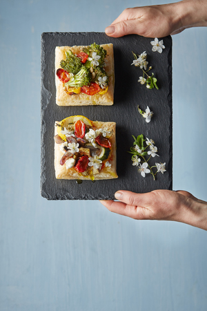 a vertical overhead of square puff pastry pieces with vegetable topping decorated with cherry blossom served on the black granite pavingの写真素材